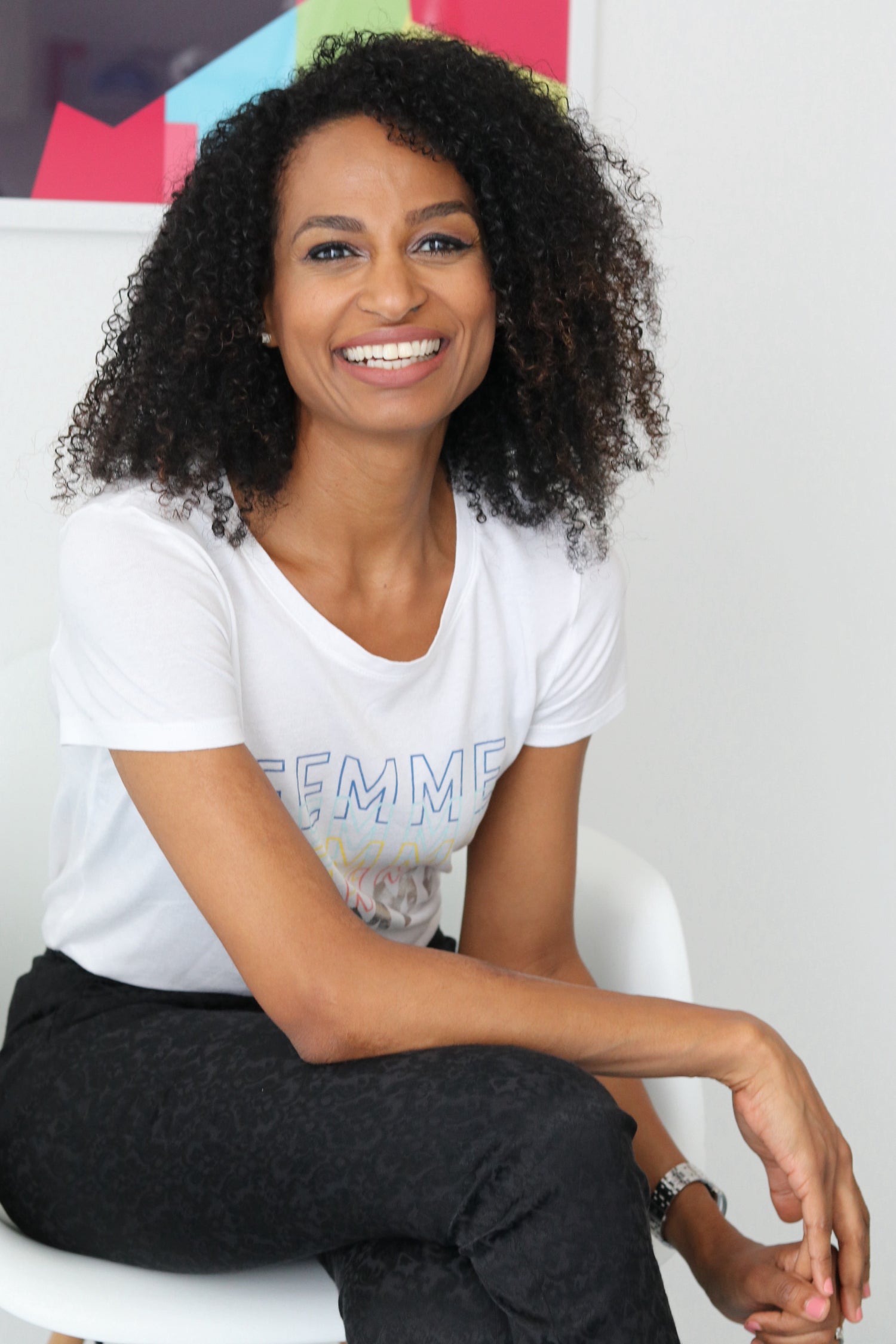 a picture of a beautiful africa lady wearing a white tshirt and black trousers sitting down and smiling towards the camera